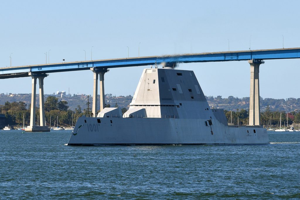 A Navy ship sails under a bridge