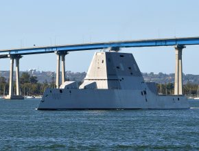A Navy ship sails under a bridge