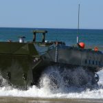 wheeled military vehicle driving out of the water onto a beach