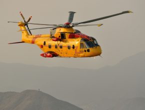 yellow helicopter flies above mountains in the haze