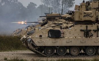 a row of tracked combat vehicles firing weapons
