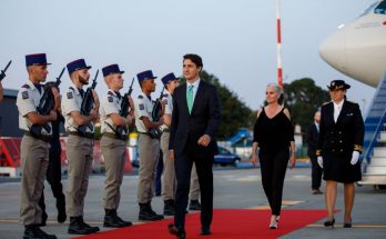 justin trudeau walks on a red carpet in front of a military guard