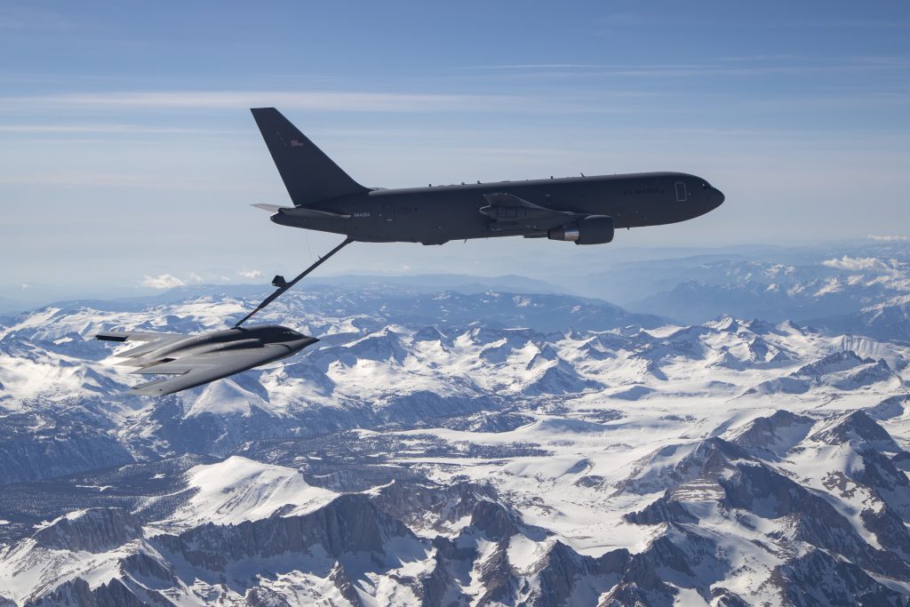 a bomber aircraft is refueled midair above snow-capped mountains