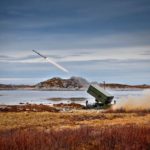 a missile is fired from a launcher on the ground near water and rocky terrain