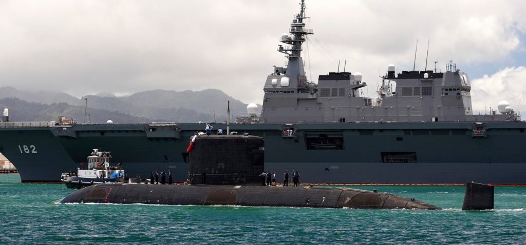 a submarine sails in front of a surface warship