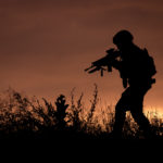 Silhouette of a soldier walking through the grass at sunset
