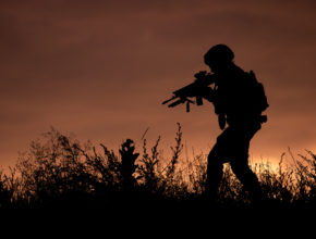Silhouette of a soldier walking through the grass at sunset