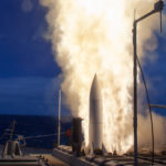 Exhaust flames shoot out alongside a missile being launched from a ship