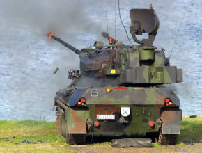 an anti-aircraft tank sits near the water firing into the air