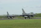 Two fighter jets line up on a runway near a grassy field
