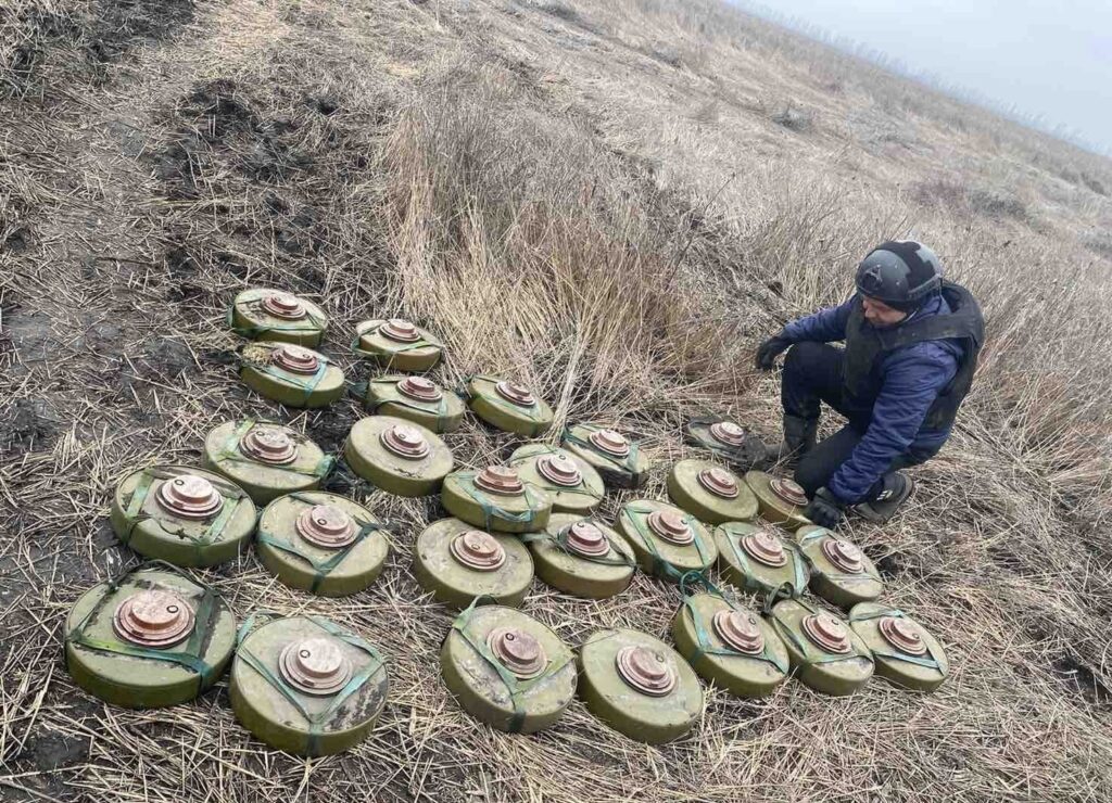a person kneels next to unexploded landmines