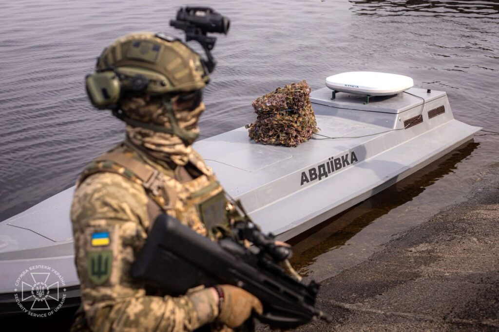 a soldier stands in front of a small unmanned naval vessel