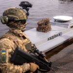 a soldier stands in front of a small unmanned naval vessel