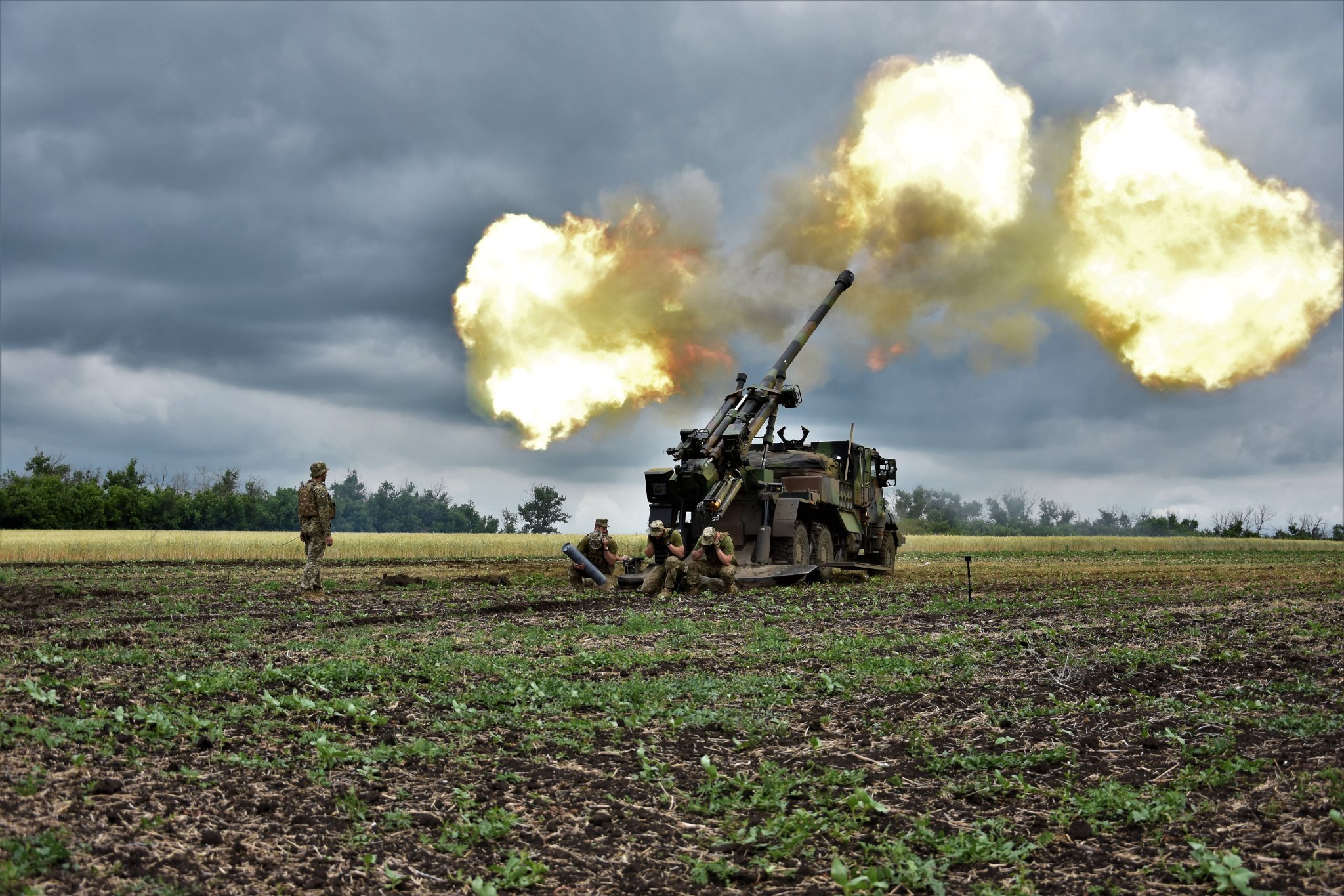 flames erupt from the barrel of a howitzer being fired in a field