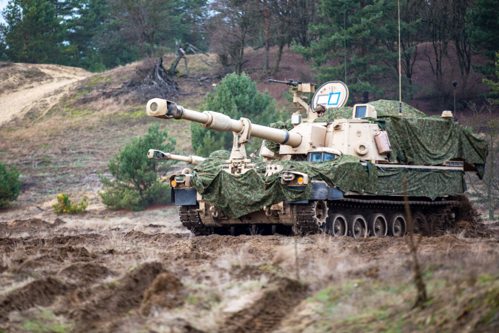 A camouflaged howitzer sits on a hill 