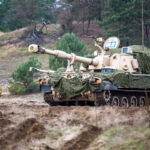 A camouflaged howitzer sits on a hill