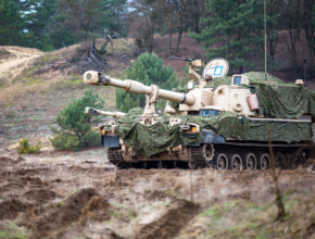 A camouflaged howitzer sits on a hill