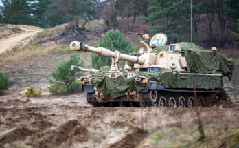 A camouflaged howitzer sits on a hill