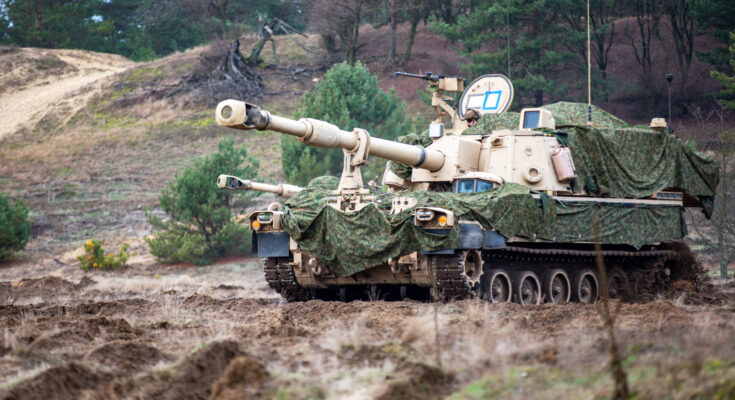 A camouflaged howitzer sits on a hill