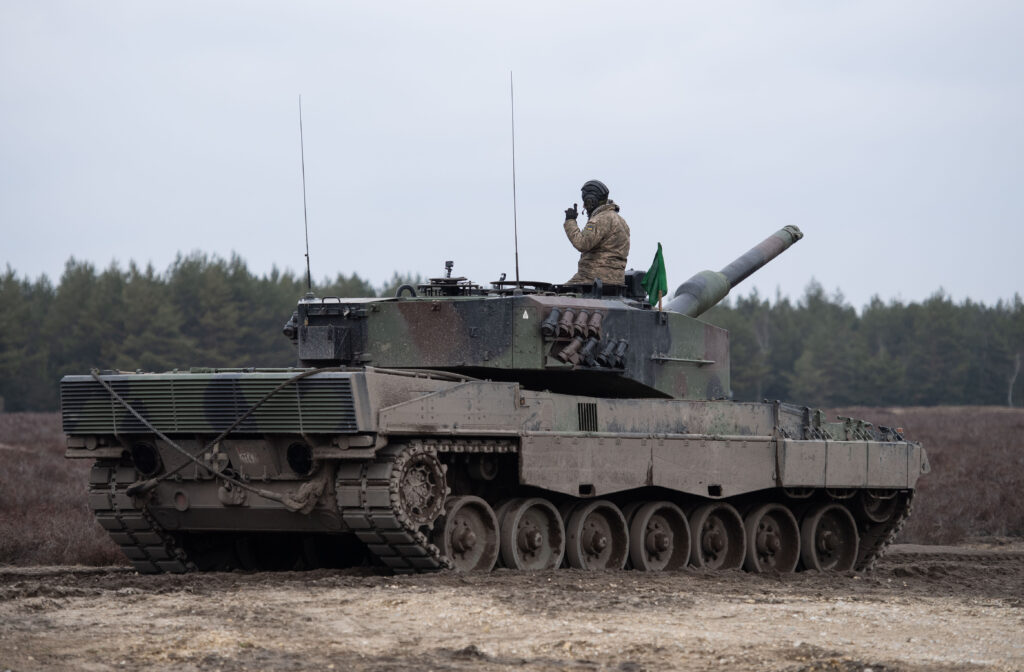 a soldier sits atop a mud-covered tank