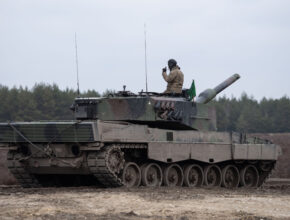 a soldier sits atop a mud-covered tank