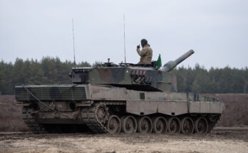 a soldier sits atop a mud-covered tank