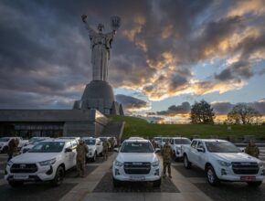 soldiers stand next to pickup trucks as the sun sets