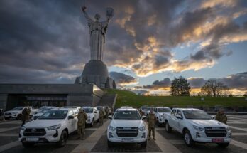 soldiers stand next to pickup trucks as the sun sets