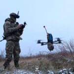 a soldier operates a small quadcopter drone carrying an explosive