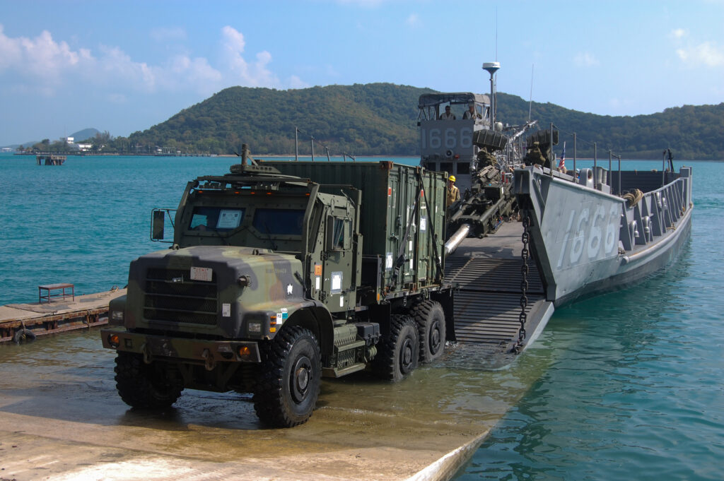 a military truck drives onto shore from a landing craft