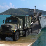 a military truck drives onto shore from a landing craft