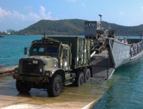 a military truck drives onto shore from a landing craft