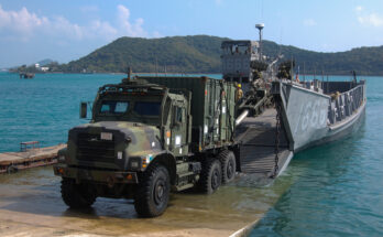 a military truck drives onto shore from a landing craft