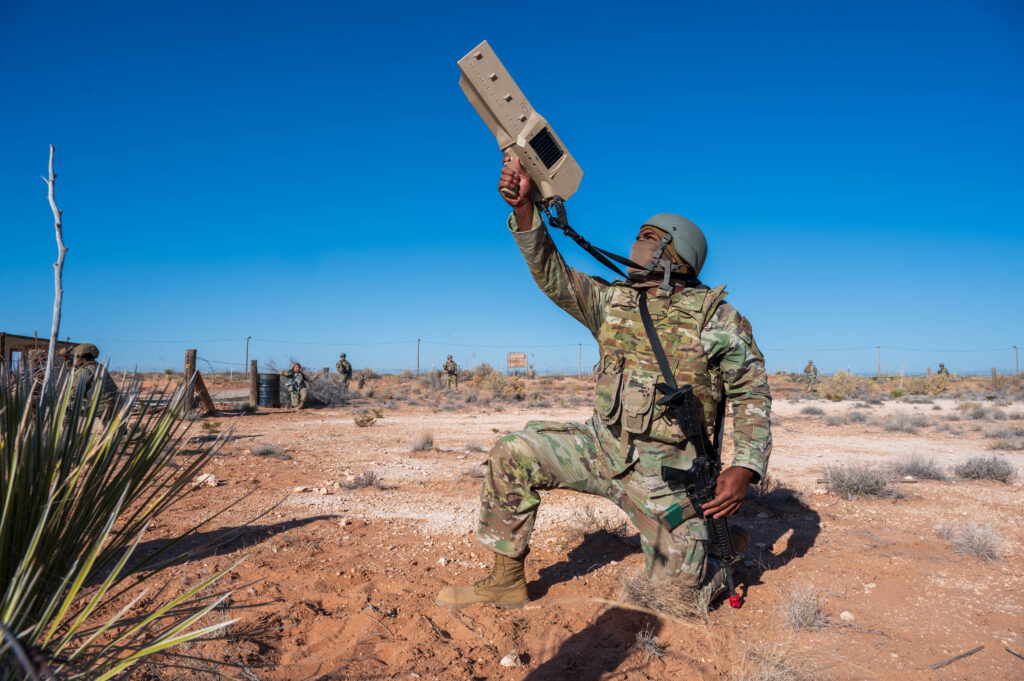 a kneeling soldier aims a counter-drone system towards the sky