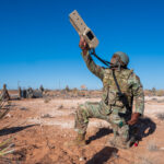 a kneeling soldier aims a counter-drone system towards the sky