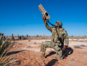 a kneeling soldier aims a counter-drone system towards the sky