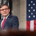 The Speaker of the House stands in front of an American flag