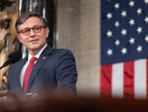 The Speaker of the House stands in front of an American flag