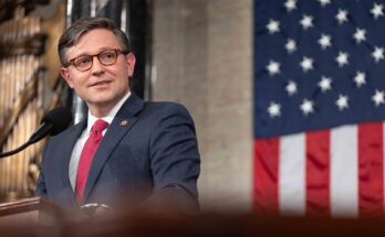 The Speaker of the House stands in front of an American flag