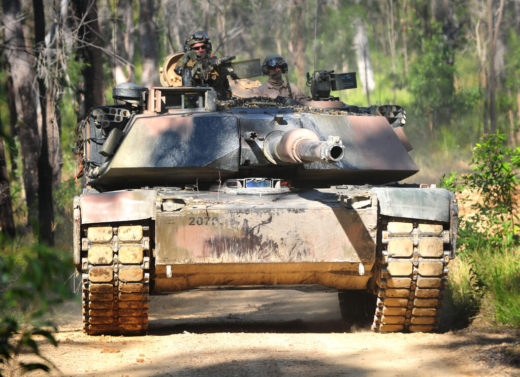 A tank drives down a dirt path in a forest
