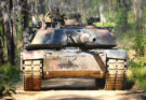 A tank drives down a dirt path in a forest