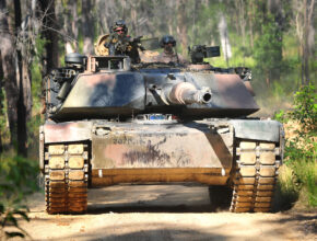 A tank drives down a dirt path in a forest
