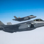 A pair of fighter jets fly above the clouds