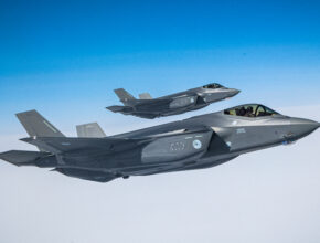 A pair of fighter jets fly above the clouds